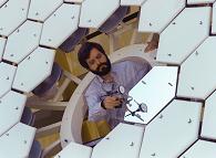 An array of hexagonal mirrors with a man measuring the mirrors.